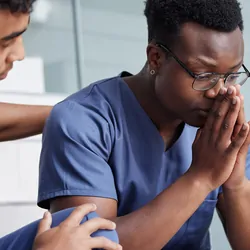 A stressed health care worker being comforted by a colleague