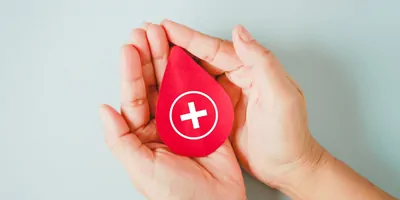 Person's hands holding a red foam stress ball that is in the shape of a blood droplet