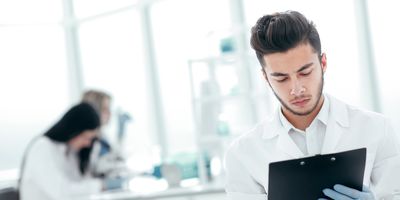 Photo of a clinical lab professional holding a clip board conducting a lab inspection.