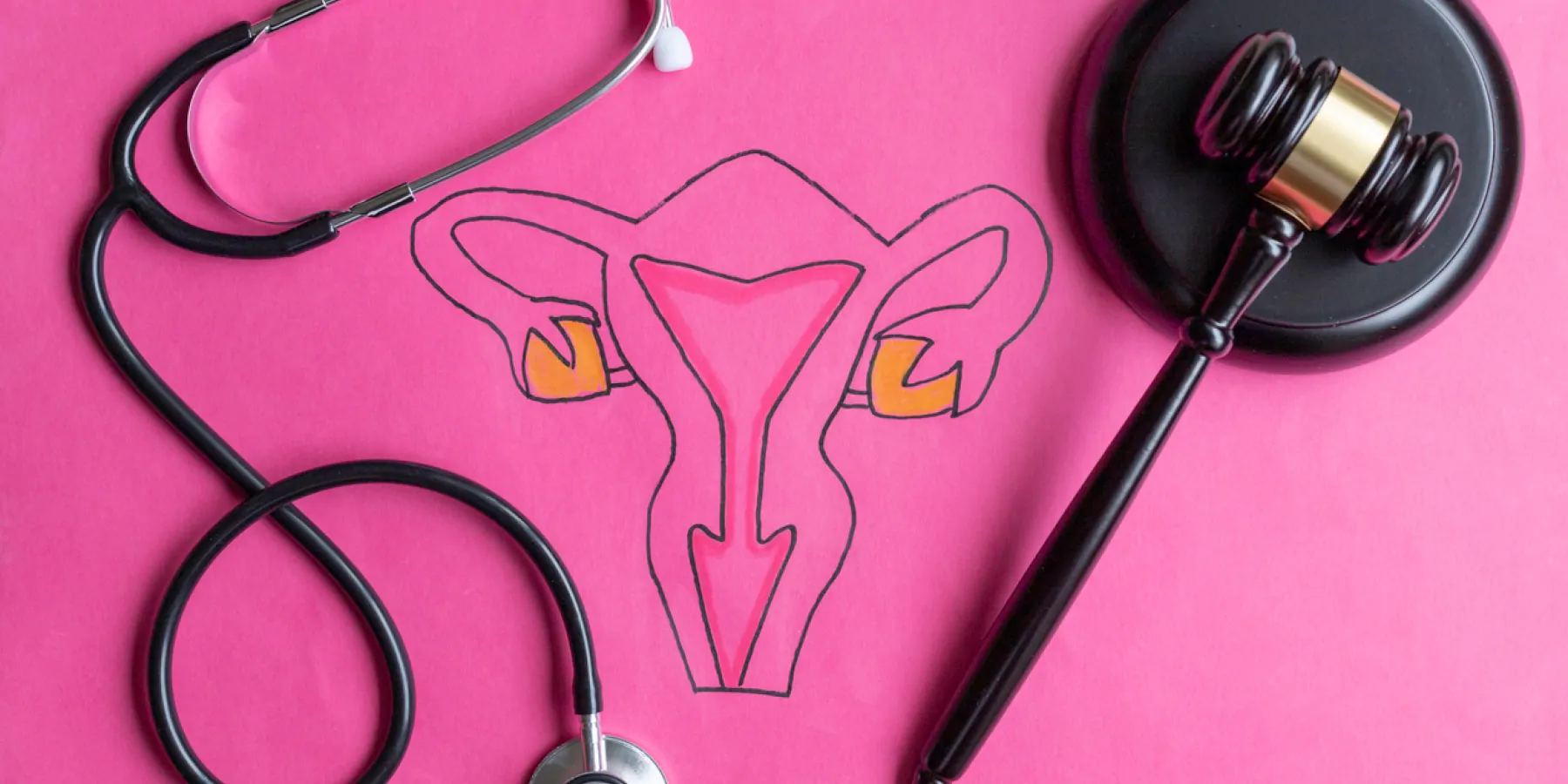 A gavel and a stethoscope on a pink table with female reproductive organs drawn on it