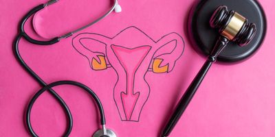 A gavel and a stethoscope on a pink table with female reproductive organs drawn on it