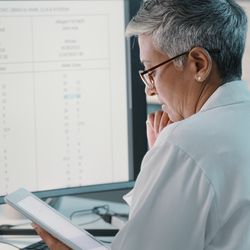 Women wearing white lab coats look at monitor of data with microscope sitting nearby.