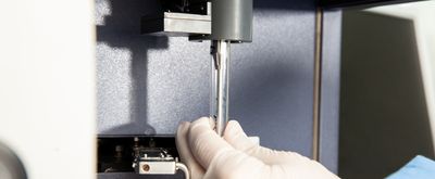 Lab worker with white gloves inserts glass tube with sample into flow cytometry machine