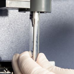 Lab worker with white gloves inserts glass tube with sample into flow cytometry machine