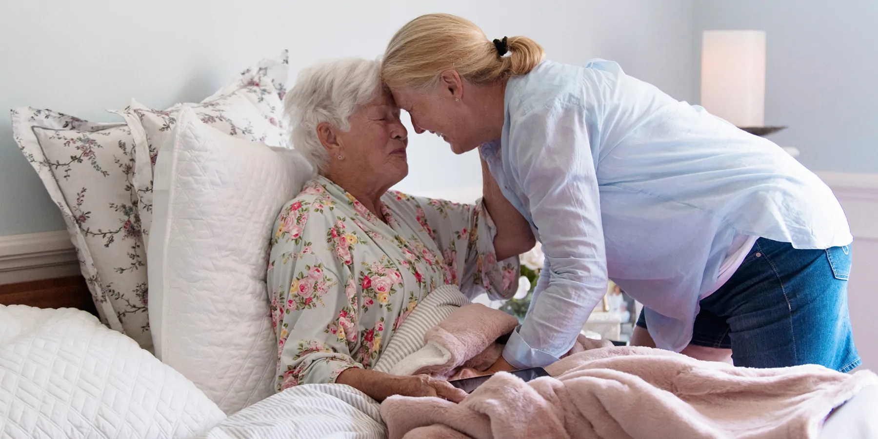 A senior woman in her bed embracing her daughter with emotion