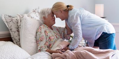 A senior woman in her bed embracing her daughter with emotion