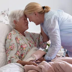A senior woman in her bed embracing her daughter with emotion