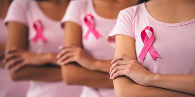 Three young multiracial women stand in a single file wearing pink ribbons to denote breast cancer.