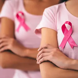Three young multiracial women stand in a single file wearing pink ribbons to denote breast cancer.