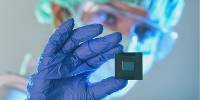 Close-up of a lab personnel in PPE holding a microfluidic chip in hand.