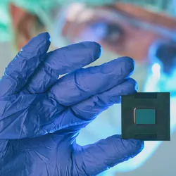 Close-up of a lab personnel in PPE holding a microfluidic chip in hand.