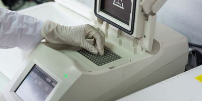 Close-up of technician with gloved hand placing sample vials into a PCR thermocycler.