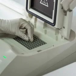 Close-up of technician with gloved hand placing sample vials into a PCR thermocycler.