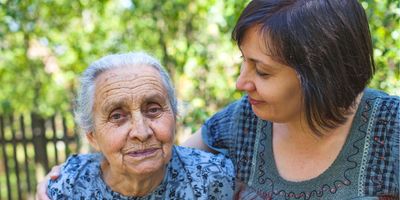  A middle-aged woman posing with her old mother with a garden in the background.