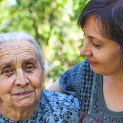 A middle-aged woman posing with her old mother with a garden in the background.