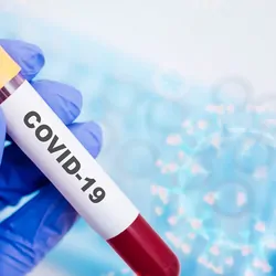 A gloved hand holds COVID-19 blood sample in a vacutainer with virus background.