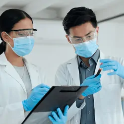 Close-up of a female and a male researcher with PPE reviewing a test sample together