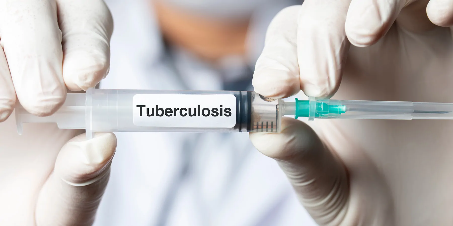 Close-up of a pair of gloved hands holding a syringe with Tuberculosis written.