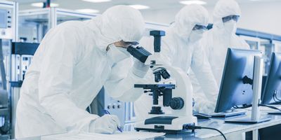 Laboratory scientists in PPE Doing Research, using a microscope and writing data in a notebook