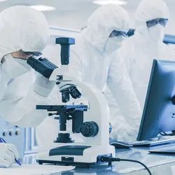 Laboratory scientists in PPE Doing Research, using a microscope and writing data in a notebook