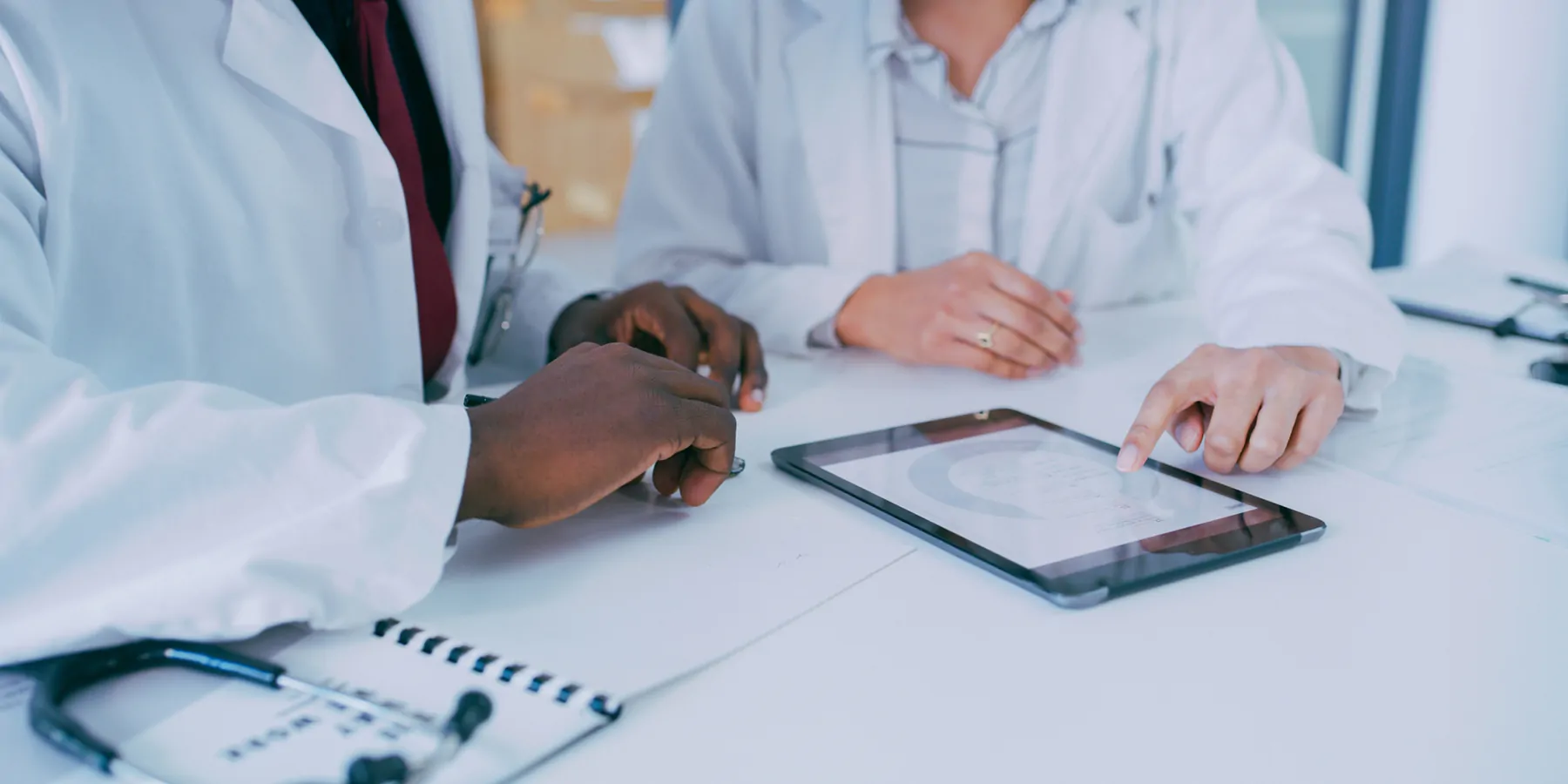 Close-up of two clinicians using a digital tablet during a discussion in a lab space.