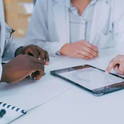 Close-up of two clinicians using a digital tablet during a discussion in a lab space.