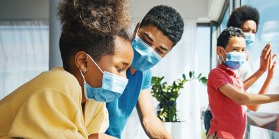 Family of four, wearing face masks, looking through a window while under home isolation/quarantine during COVID-19 pandemic.