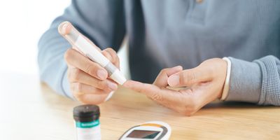 Close-up of a man using a lancet on his pointer for checking blood sugar level with a glucometer.