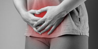 A black-and-white photo of a woman holding her genital area in pain, which is highlighted in red.