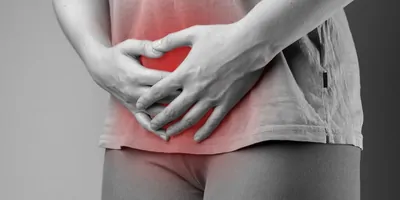 A black-and-white photo of a woman holding her genital area in pain, which is highlighted in red.