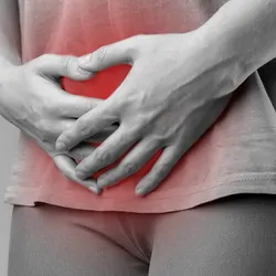 A black-and-white photo of a woman holding her genital area in pain, which is highlighted in red.