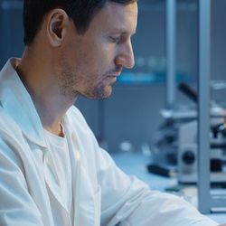 Photograph of lab personnel in a lab coat viewing a desktop in the lab that is displaying some obscured information in a graphical format.