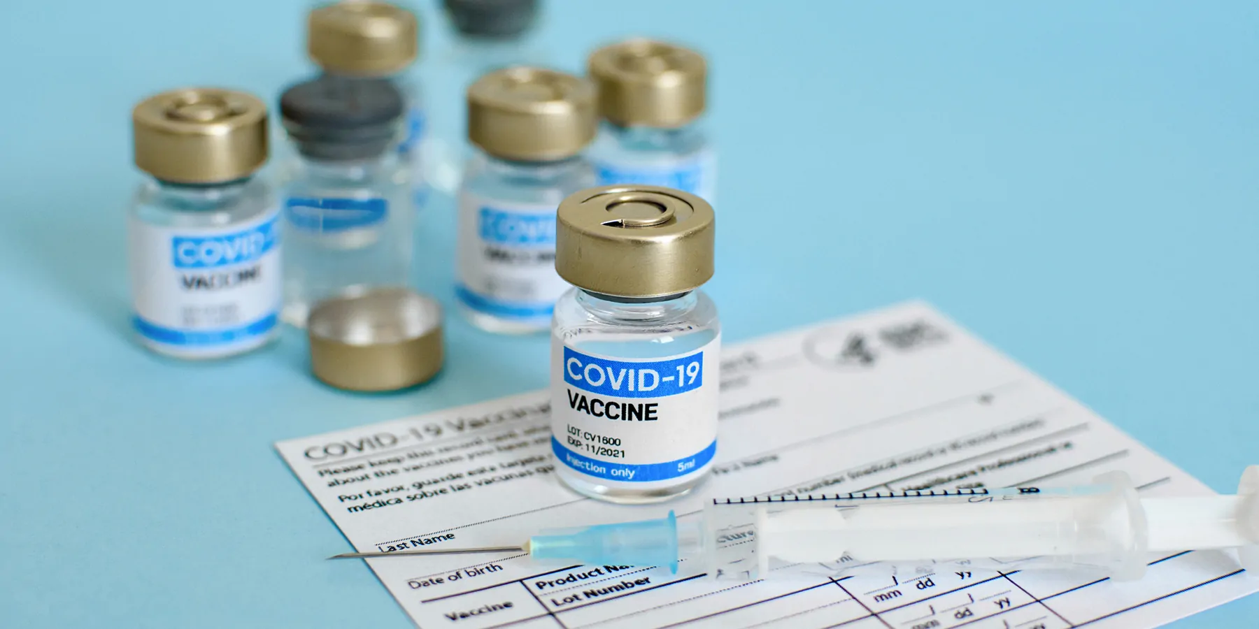 COVID-19 vaccine vial and syringe on a CDC-vaccination record card on blue background.