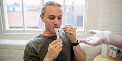 Close-up of an unrecognisable mature caucasian health professional wearing gloves handing a young male a test tube for him to collect his saliva in.