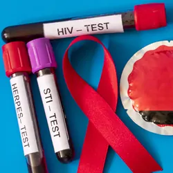 A red ribbon, symbolizing AIDS awareness, with blood tubes from sexually transmitted disease tests and a condom on blue background