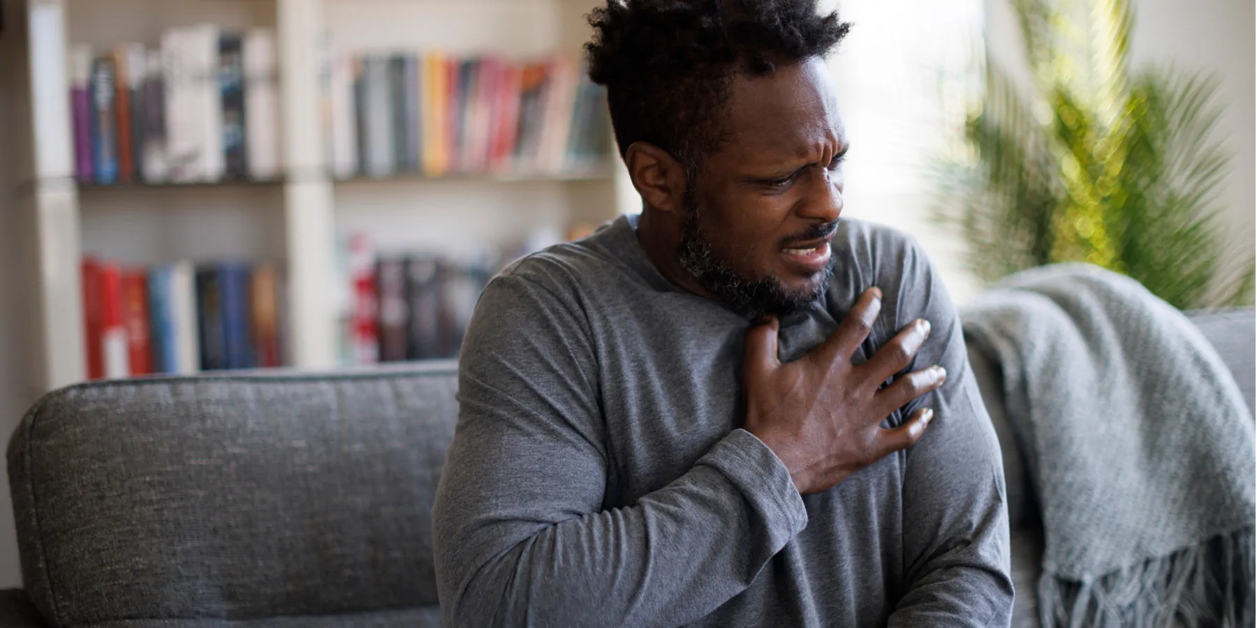 Close-up of a Black man wincing from chest pain and touching his heart area with his right hand