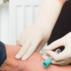 An elderly patient is being prepared for a blood test by a phlebotomist.
