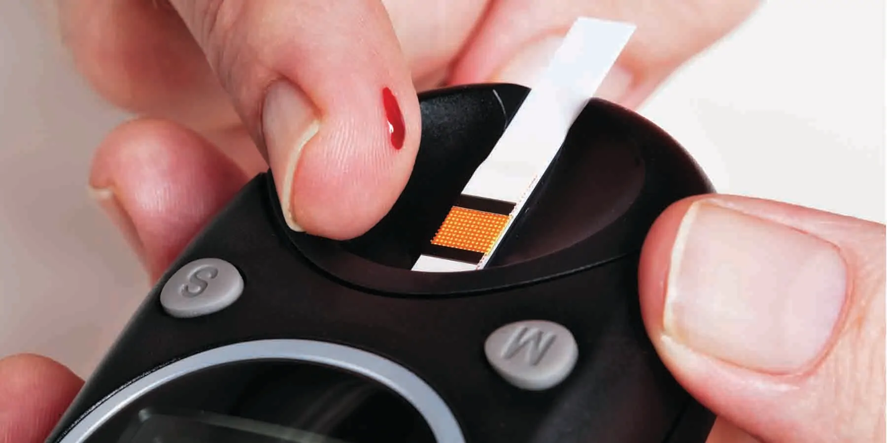 Close-up view of hands about to add a blood drop to the test strip in a glucometer