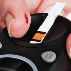 Close-up view of hands about to add a blood drop to the test strip in a glucometer