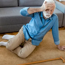 Senior man with walking stick lying on carpet at home. faint, stroke, accident or other health problem