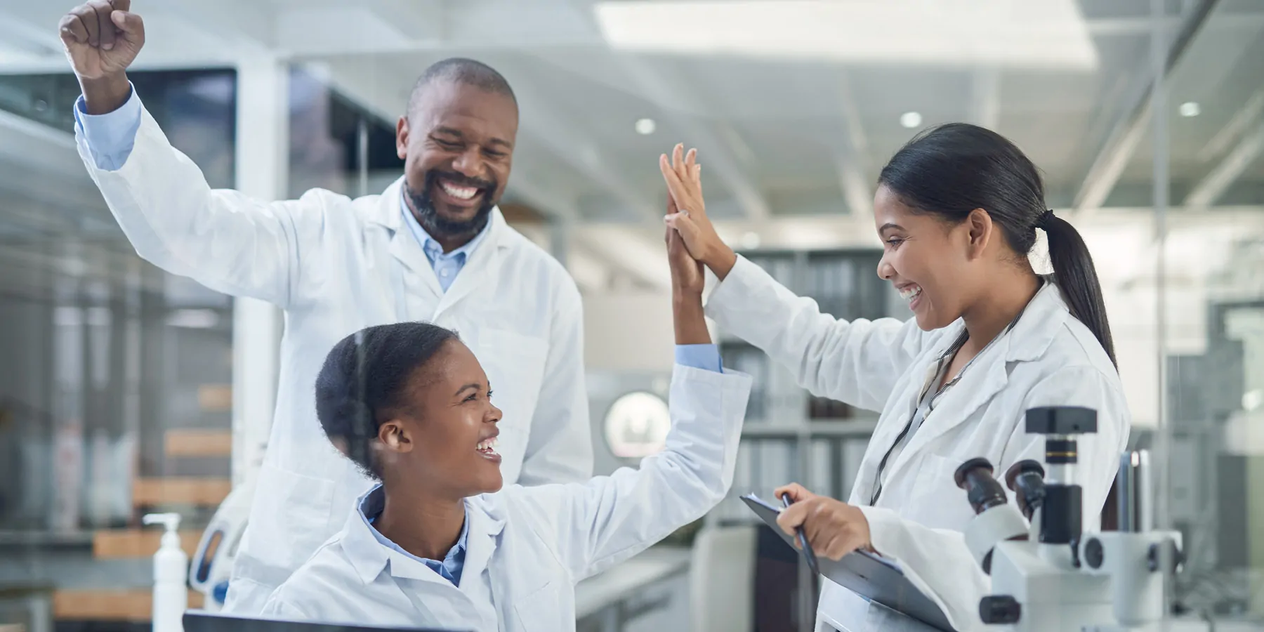 Shot of a group of young scientists giving each other a high-five while using a laptop in a laboratory