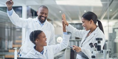 Shot of a group of young scientists giving each other a high-five while using a laptop in a laboratory
