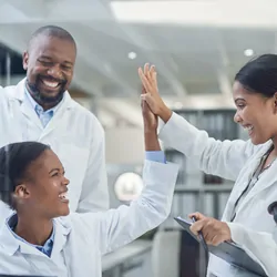 Shot of a group of young scientists giving each other a high-five while using a laptop in a laboratory