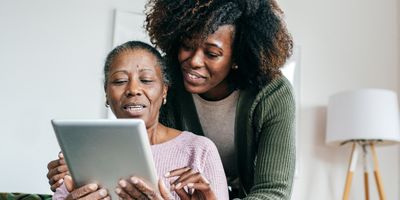 Young woman guides an older woman who holds an iPad or tablet in her hands. 
