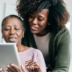 Young woman guides an older woman who holds an iPad or tablet in her hands. 