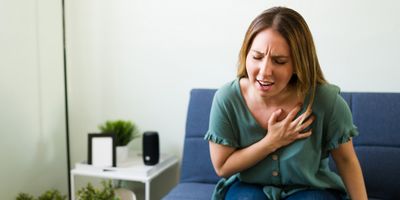 Young woman in agony with bad chest pain having a heart attack while sitting on the couch.