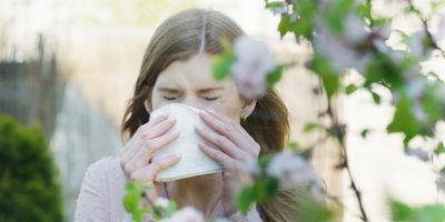A woman allergic to flowers sneezes and wipes her nose with a handkerchief in the garden.