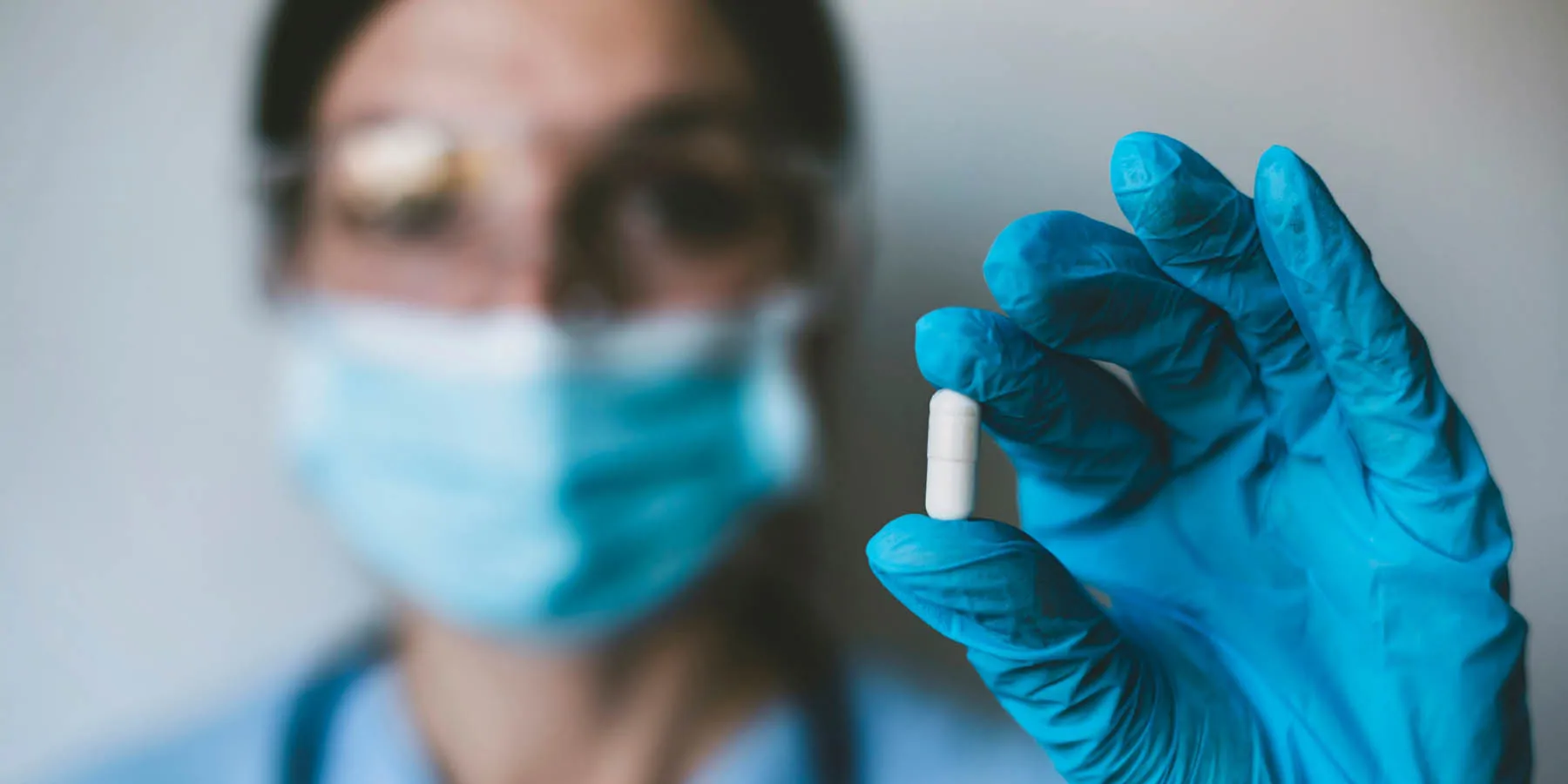 Close-up of a clinician wearing PPE holding a drug capsule