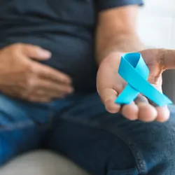 A man holding a blue prostate cancer awareness ribbon in hand