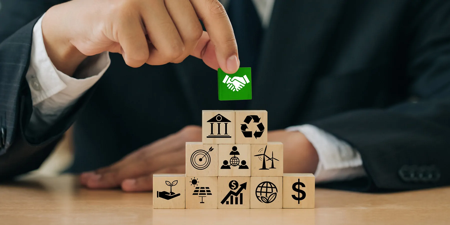 A person holds green wooden blocks with handshake icons standing with other ESG icons of sustainable development.